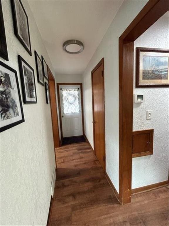 hallway featuring baseboards, dark wood-style flooring, and a textured wall