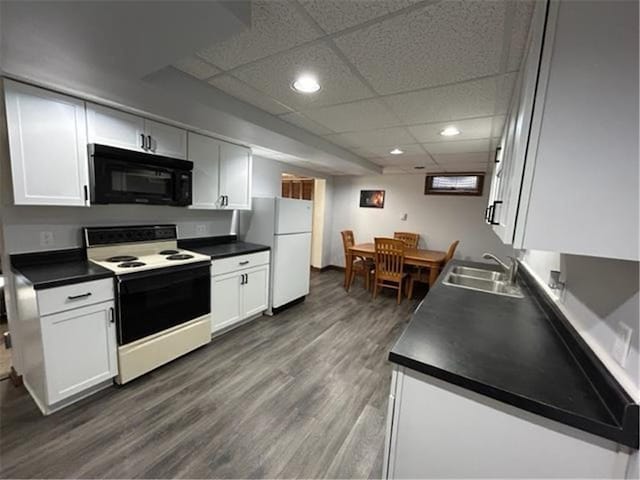 kitchen with dark countertops, white appliances, white cabinetry, and a sink