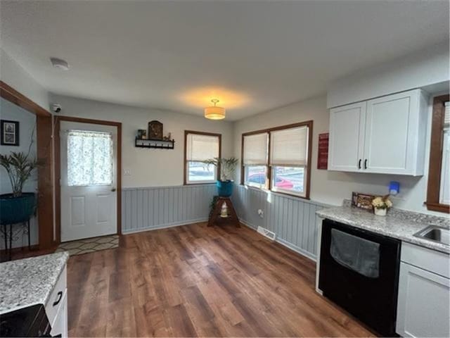 kitchen featuring dark wood-type flooring, wainscoting, white cabinets, light stone countertops, and dishwasher