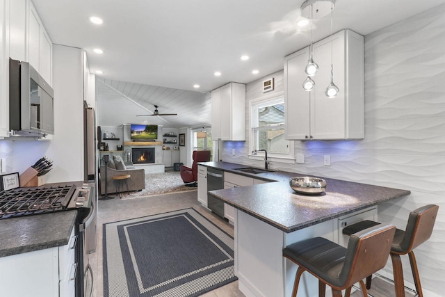 kitchen with appliances with stainless steel finishes, a breakfast bar, pendant lighting, white cabinetry, and kitchen peninsula