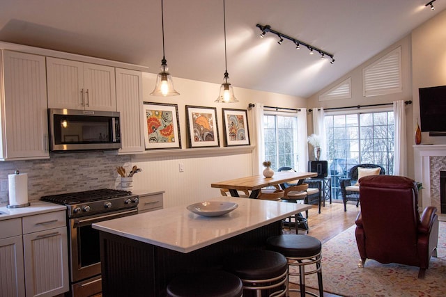 kitchen featuring hanging light fixtures, a kitchen island, stainless steel appliances, a kitchen bar, and vaulted ceiling