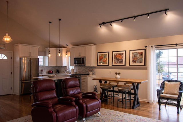 interior space featuring hardwood / wood-style floors, lofted ceiling, white cabinets, hanging light fixtures, and high end appliances