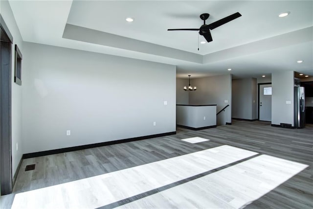 unfurnished living room with a tray ceiling, dark hardwood / wood-style flooring, and ceiling fan with notable chandelier