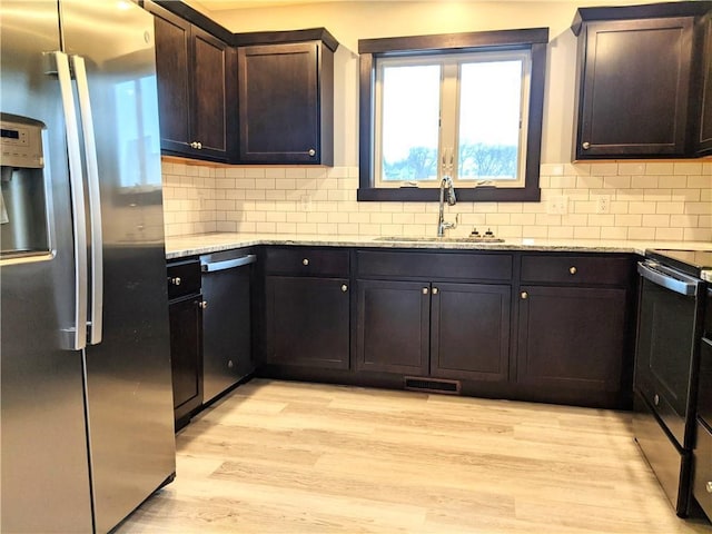 kitchen featuring sink, appliances with stainless steel finishes, light stone counters, dark brown cabinetry, and light wood-type flooring