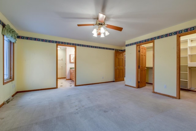 unfurnished bedroom featuring ceiling fan, a spacious closet, light carpet, and ensuite bath