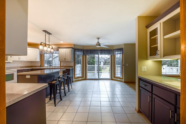 kitchen featuring a breakfast bar area, ceiling fan, stove, backsplash, and dark brown cabinetry