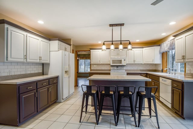 kitchen featuring a breakfast bar, sink, white cabinets, a center island, and white appliances