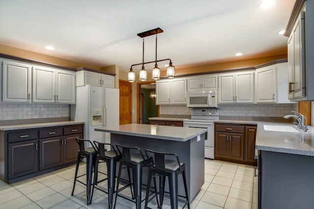 kitchen with light tile patterned flooring, a kitchen island, sink, a breakfast bar area, and white appliances