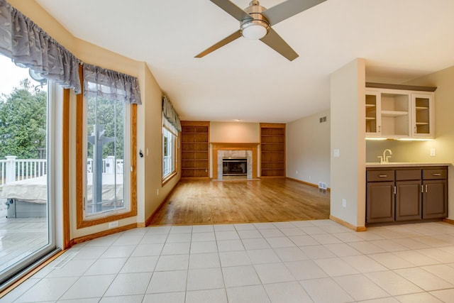 unfurnished living room with sink, light tile patterned floors, built in features, ceiling fan, and a fireplace