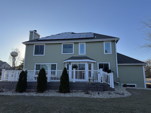 back of house with a deck and solar panels