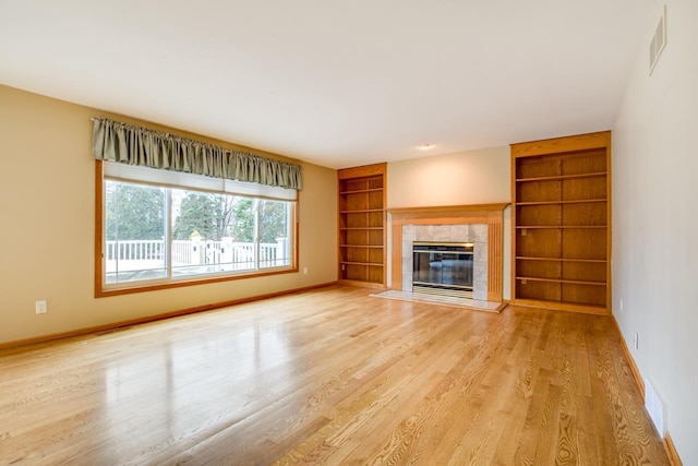 unfurnished living room with built in shelves, a tiled fireplace, and light wood-type flooring