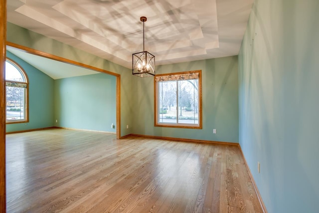 spare room featuring a chandelier, light wood-type flooring, and a tray ceiling