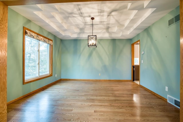 unfurnished dining area with hardwood / wood-style floors, a tray ceiling, and a notable chandelier