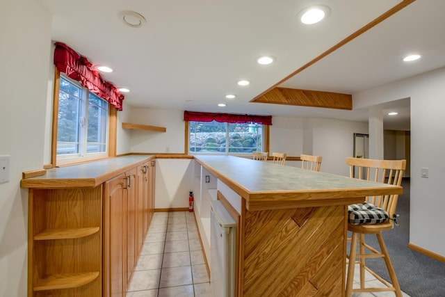 kitchen featuring light tile patterned flooring, a healthy amount of sunlight, a kitchen bar, and kitchen peninsula