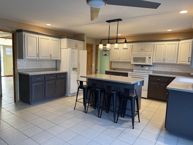 kitchen featuring light tile patterned flooring, a kitchen island, sink, a kitchen bar, and white appliances