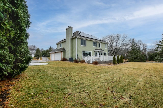 rear view of property with a yard, a wooden deck, solar panels, central air condition unit, and a garage