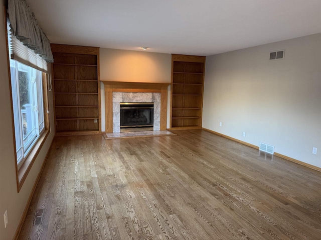 unfurnished living room featuring built in shelves, a premium fireplace, and light hardwood / wood-style flooring