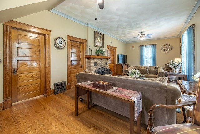 living room featuring crown molding, ceiling fan, a fireplace, and light hardwood / wood-style flooring