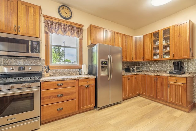 kitchen with stainless steel appliances, light stone counters, backsplash, and light wood-type flooring