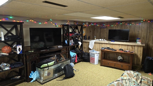 living room with carpet flooring, a drop ceiling, and wood walls