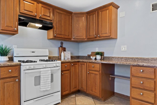 kitchen featuring built in desk, light tile patterned floors, dark stone counters, and gas range gas stove