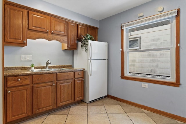 kitchen with white refrigerator, light tile patterned flooring, sink, and dark stone counters