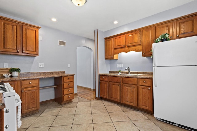 kitchen featuring dark stone countertops, sink, white appliances, and light tile patterned floors