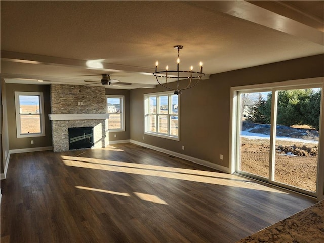 unfurnished living room with dark wood-type flooring, a stone fireplace, ceiling fan with notable chandelier, and beamed ceiling