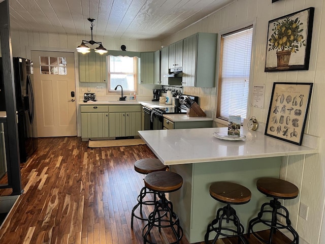 kitchen with black refrigerator, a breakfast bar, sink, green cabinets, and electric range