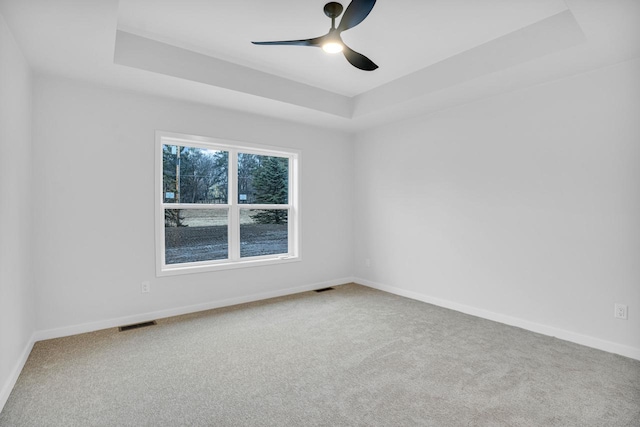 empty room with a raised ceiling, carpet flooring, and ceiling fan