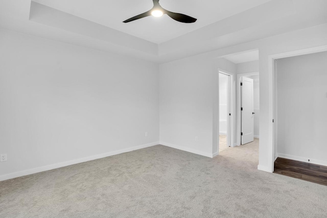 empty room featuring a raised ceiling, light carpet, and ceiling fan