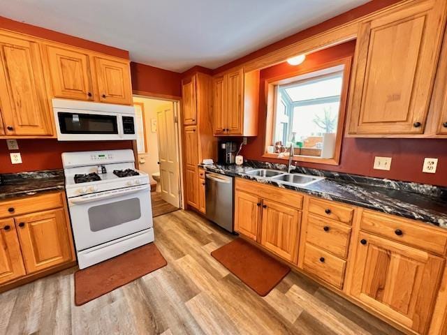 kitchen featuring sink, dark stone countertops, white appliances, and light wood-type flooring