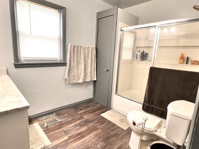 full bathroom with vanity, hardwood / wood-style floors, bath / shower combo with glass door, and toilet