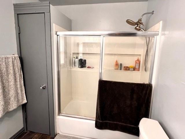 bathroom with enclosed tub / shower combo, hardwood / wood-style floors, and toilet