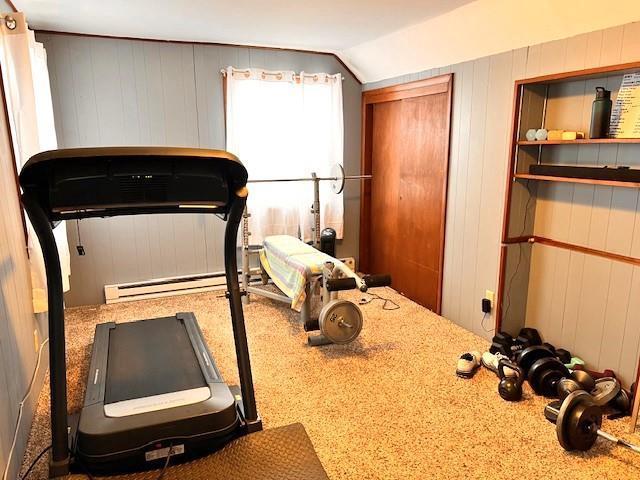 exercise room featuring vaulted ceiling, a baseboard heating unit, and wood walls