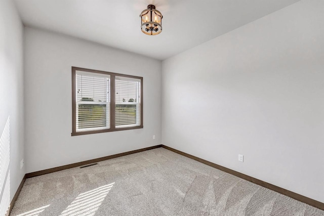 spare room featuring light colored carpet and a chandelier