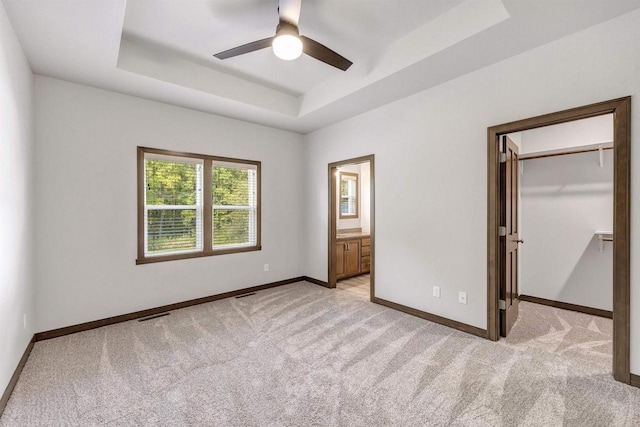 unfurnished bedroom featuring light carpet, a spacious closet, ensuite bath, and a raised ceiling