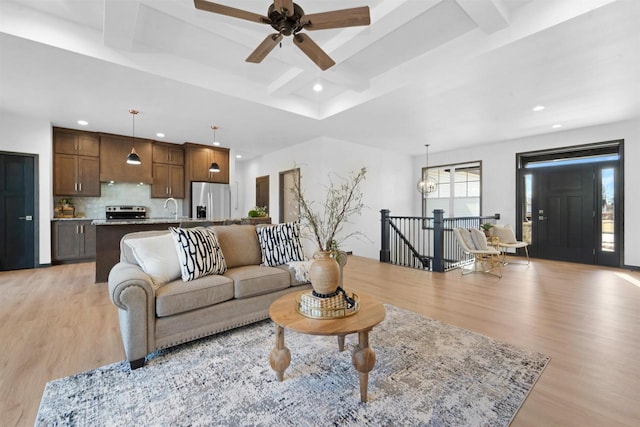 living room featuring beam ceiling, a chandelier, sink, and light hardwood / wood-style flooring