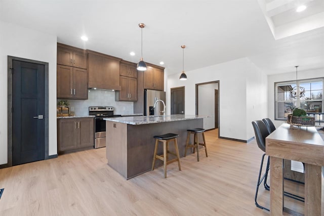 kitchen with pendant lighting, appliances with stainless steel finishes, backsplash, light stone countertops, and an island with sink