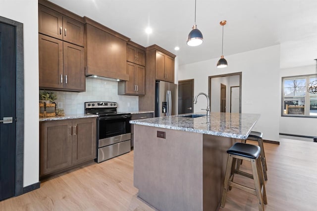 kitchen with hanging light fixtures, appliances with stainless steel finishes, sink, and a center island with sink