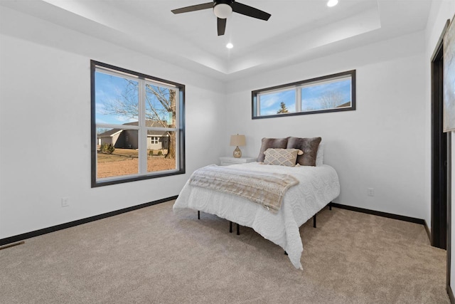 bedroom featuring ceiling fan, a raised ceiling, and light carpet