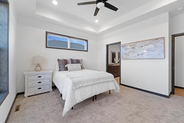 bedroom with light carpet, a raised ceiling, ceiling fan, and ensuite bathroom