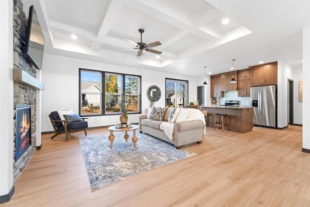 living room featuring coffered ceiling, a fireplace, light hardwood / wood-style floors, and ceiling fan