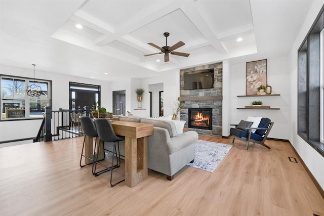 living room featuring a stone fireplace, coffered ceiling, an inviting chandelier, and light wood-type flooring