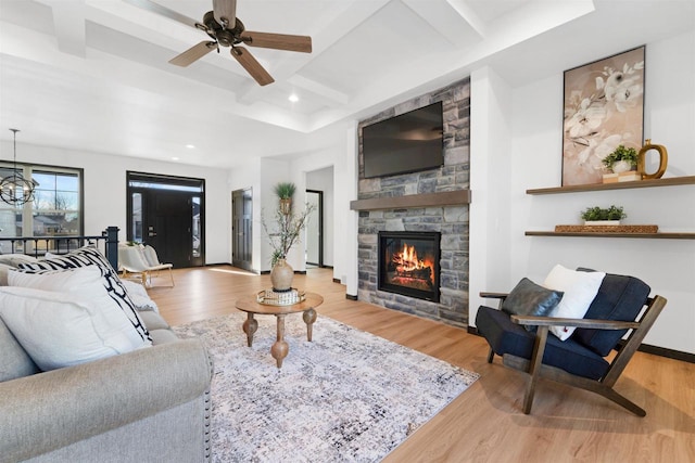 living room featuring coffered ceiling, a stone fireplace, light hardwood / wood-style flooring, beamed ceiling, and ceiling fan with notable chandelier