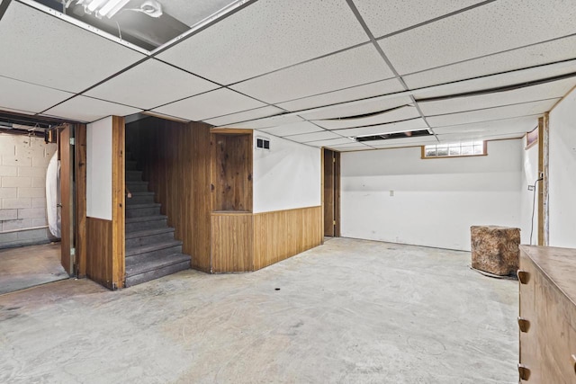 basement featuring a drop ceiling and wooden walls