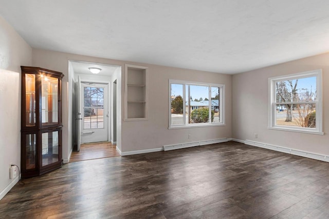 empty room featuring baseboard heating, built in shelves, and dark wood-type flooring