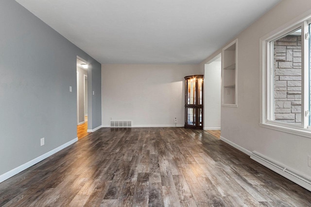 empty room with dark wood-type flooring and a baseboard heating unit