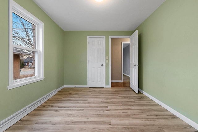 unfurnished bedroom featuring a baseboard heating unit and light wood-type flooring