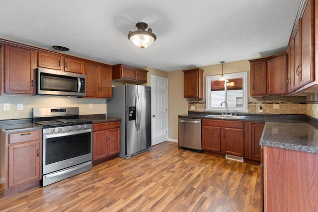 kitchen featuring appliances with stainless steel finishes, decorative light fixtures, sink, backsplash, and dark wood-type flooring